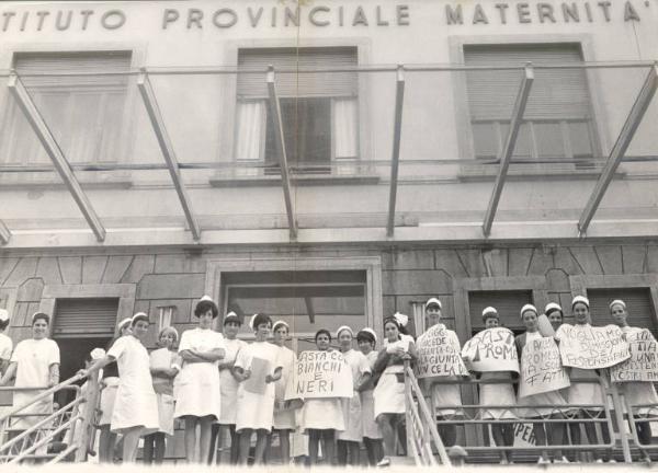 Milano - Sciopero infermiere - Macedonia Melloni - Presidio delle lavoratrici davanti all'ingresso dell'ospedale - Ritratto di gruppo - Infermiere in camice con cartelli di protesta - Insegna "Istituto provinciale maternità"