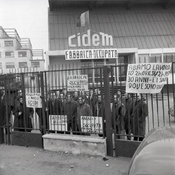 Cidem - Occupazione della fabbrica - Lavoratori dietro i cancelli - Striscione e cartelli di rivendicazione - Bandiera - Insegna Cidem