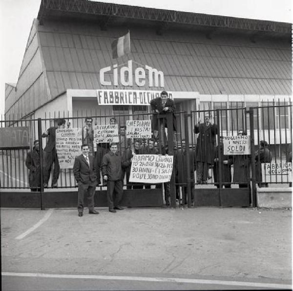 Cidem - Occupazione della fabbrica - Lavoratori dietro i cancelli - Striscione e cartelli di rivendicazione - Bandiera - Insegna Cidem