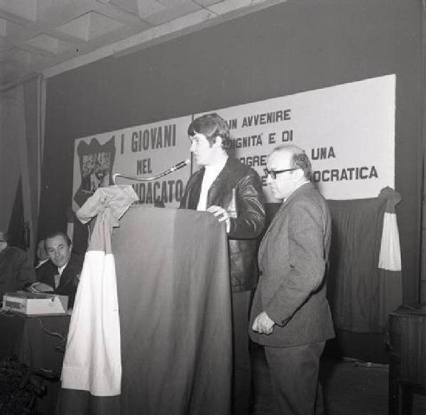 Camera del Lavoro - Salone "Di Vittorio" - Interno - Conferenza provinciale dei giovani metalmeccanici milanesi - Palco - Giovane al microfono - Striscione Fiom