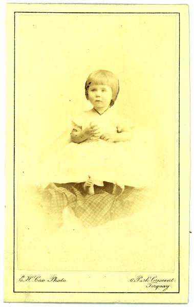 Ritratto infantile - Bambina seduta su un tessuto scozzese, a piedi nudi