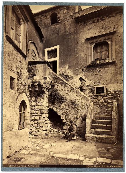 Taormina - Casa la Floresta. Veduta interna del cortile con la scalinata d'accesso e due persone.