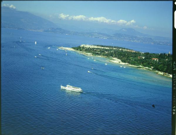 Sirmione. Navigazione sul lago. Battello. Grotte di Catullo sillo sfondo. Veduta aerea.