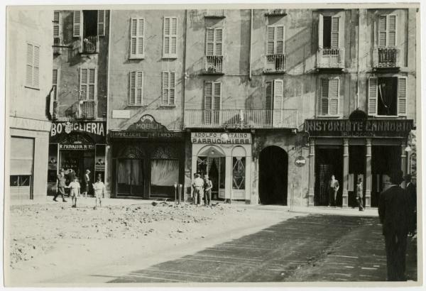 Milano - Via Paolo da Cannobio n. 9 - Negozi Bottiglieria "R. Privativa N°126", "G. Mauro Mobili Tappezzerie Materassaio", parrucchiere "Adolfo Gattaino", ristorante/alloggio "Cannobio " - Passanti e macerie