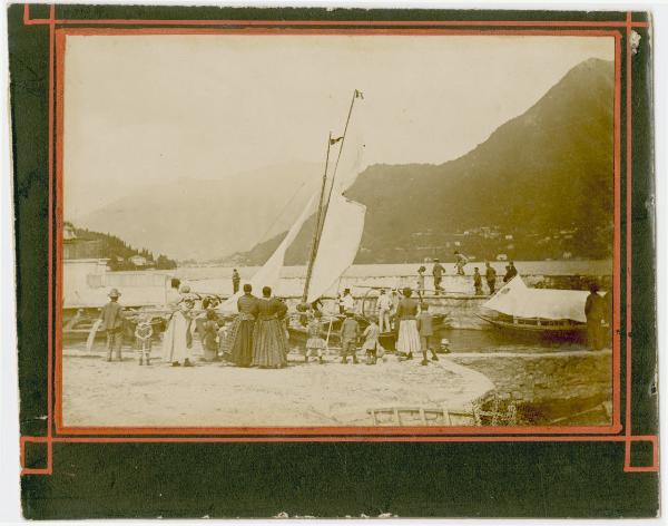 Veduta di Cernobbio (Como), il porto con l'imbarcazione di Casa Sormani, donne, uomini e bambini davanti all'imbarcazione.