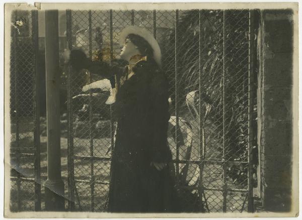 Ritratto femminile - Donna, attrice, con cappello appoggiata alla rete di un cancello - Esterno