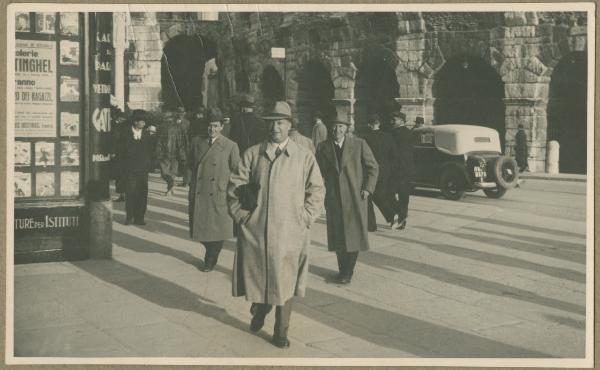 Ritratto di gruppo maschile - Antonio Boschi con altri due uomini - Verona - Arena - Esterno - Automobile - Passanti - Manifesti pubblicitari