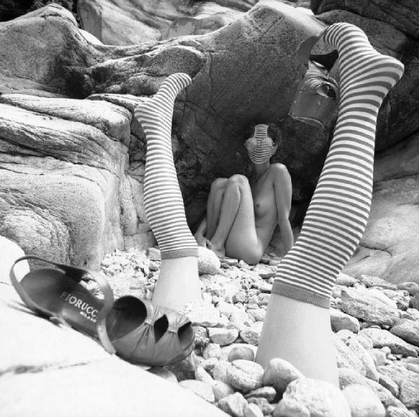 Nudo femminile - Grotte rocciose - Gambe di manichino con calze a righe - Sandali Fiorucci