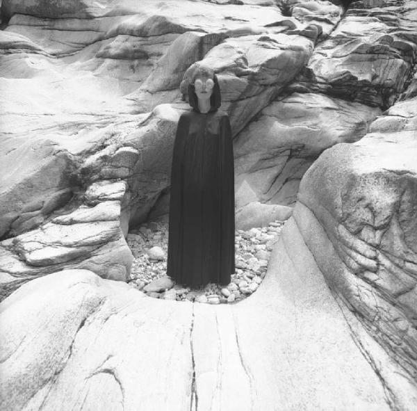Ritratto femminile - modella con mantella e occhiali formati da colini sullo sfondo di rocce