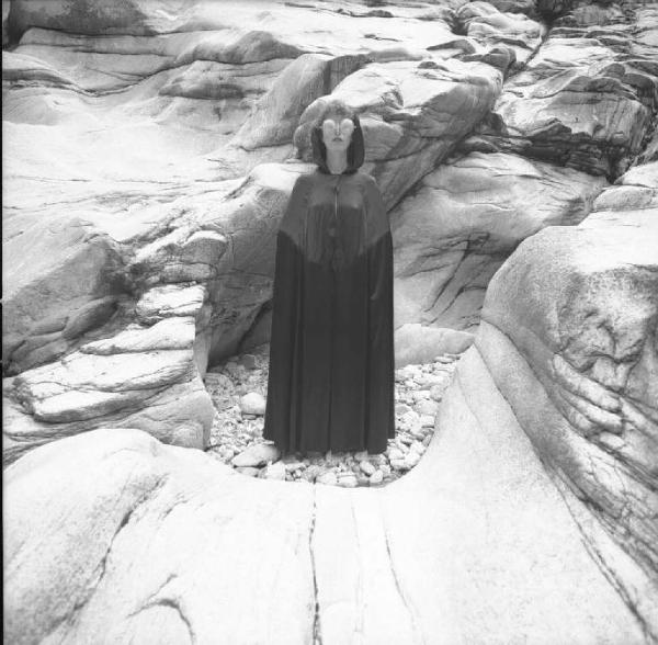 Ritratto femminile - modella con mantella e occhiali formati da colini sullo sfondo di rocce