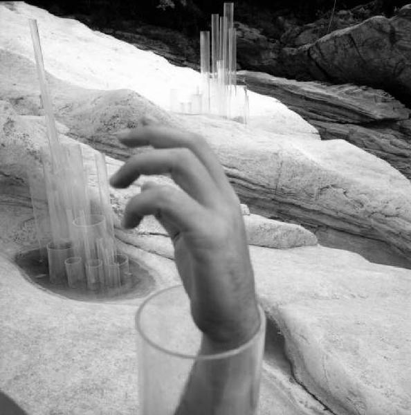 Mano maschile emerge da un tubo di un'installazione in plexiglas sullo sfondo di un paesaggio roccioso