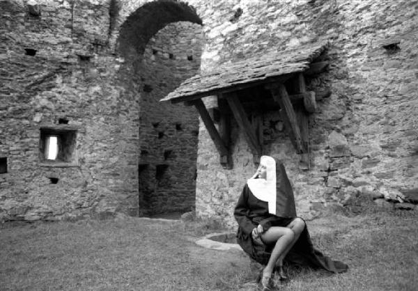 Ritratto femminile - giovane - modella travestita da suora che si abbottona una giarrettiera nel cortile di un castello. Lucy