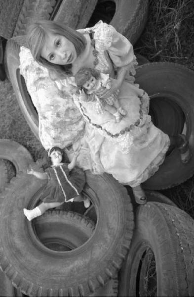 Ritratto femminile - modella Vanessa seduta su cumulo di copertoni d'auto, mentre gioca con bambole