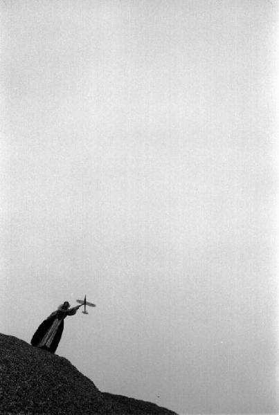 Figura femminile in lontananza su cumuli di pietre, mentre gioca con modellino di aereo. Vanessa