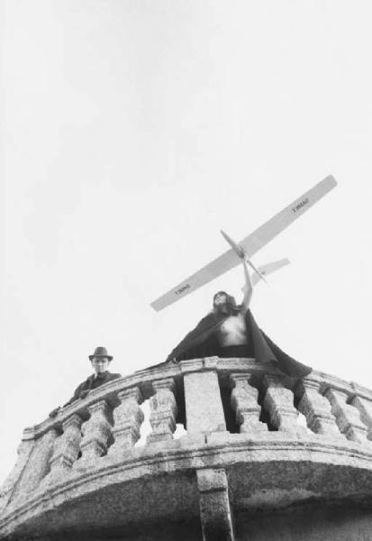 Fotomodella con modellino di aereo posa sopra il parapetto di una villa barocca - al suo fianco un anziano - esterno