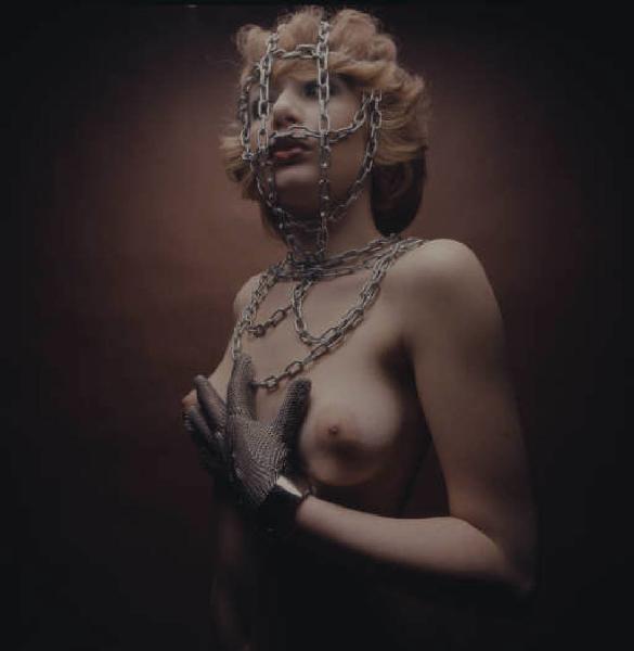 Ritratto femminile - modella in topless con catena sul volto e guanto in maglia di ferro