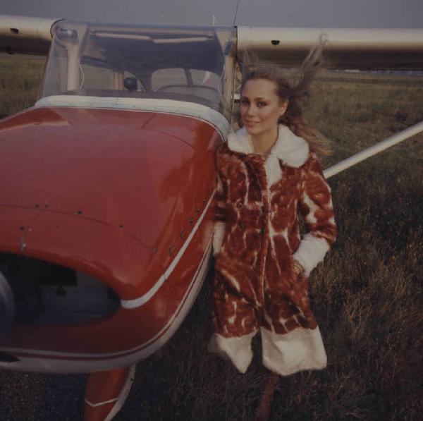 Ritratto in esterno. Fotomodella indossa una pelliccia ecologia davanti ad un aeroplano