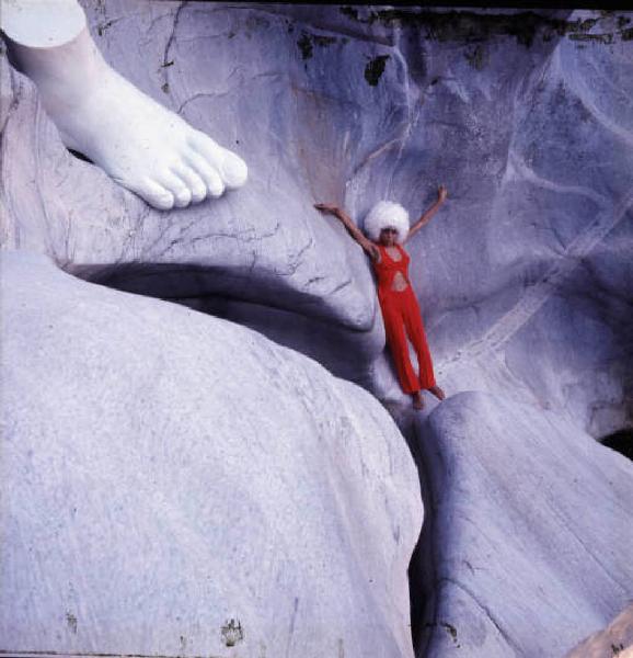 Ritratto femminile - modella tra le rocce con vestito rosso e copricapo di pelo