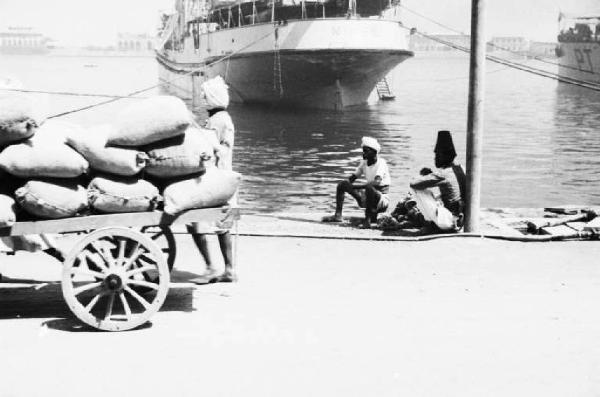 Viaggio in Africa. Massaua - porto - banchina - indigeni - carro carico di sacchi - poppa di una nave ormeggiata