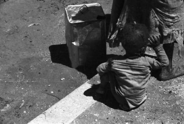 Viaggio in Africa. Nefasit - bambino indigeno seduto per strada - latta