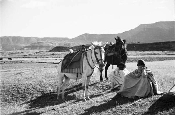 Viaggio in Africa. Due militari indigeni riposano seduti per terra accanto ai loro cavalli
