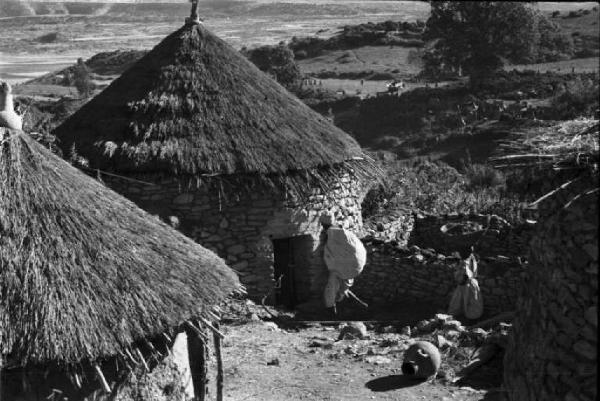 Viaggio in Africa. Paesaggio africano, villaggio con capanne dai tetti di paglia e muretti a secco. In lontannaza un indigeno con carico sulle spalle