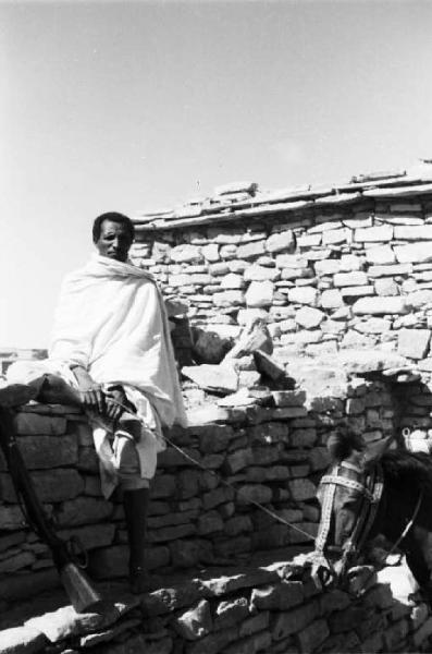 Viaggio in Africa. Indigeno seduto su un muretto in pietra tiene per le briglie un cavallo