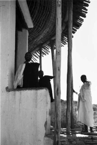 Viaggio in Africa. Indigeni all'esterno di un edificio in muratura col tetto in paglia