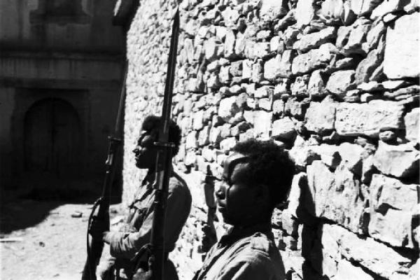 Viaggio in Africa. Due militari indigeni armati montano la guardia all'esterno di un edificio in pietra