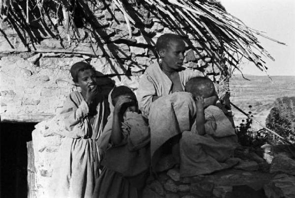 Viaggio in Africa. Ritratto di gruppo - bambini e un giovane all'esterno di un'abitazione in pietra