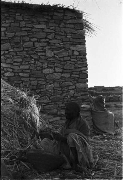 Viaggio in Africa. Indigeno seduto all'esterno di un'abitazione in pietra a fianco di un covone di paglia