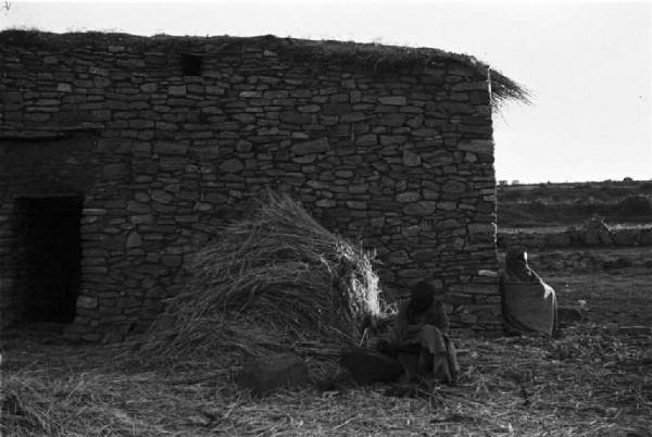 Viaggio in Africa. Indigeno seduto all'esterno di un'abitazione in pietra a fianco di un covone di paglia