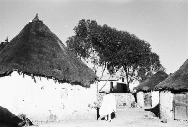 Viaggio in Africa. Scorcio di un villaggio - abitazioni circolari in calce bianca con tetto in paglia, un abitante percorre una strada sterrata