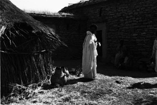 Viaggio in Africa. Donna indigena sulla soglia di una capanna vicino a delle anfore. Sullo sfondo abitazioni in pietra