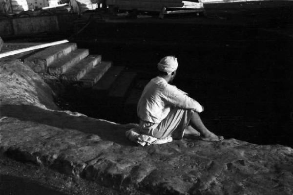 Viaggio in Africa. Massaua: portuale indigeno seduto lungo una banchina del porto durante una pausa