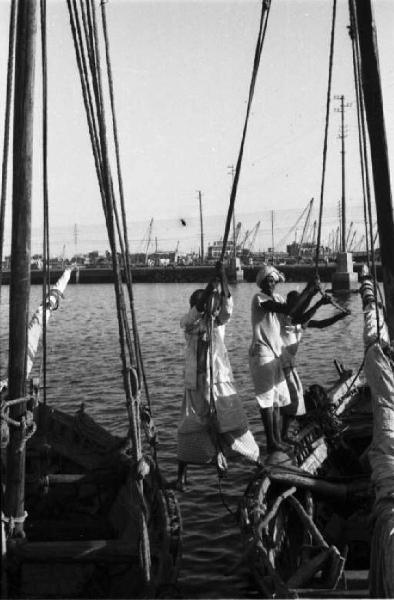 Viaggio in Africa. Massaua: scorcio del porto, portuali indigeni al lavoro su imbarcazioni a vela