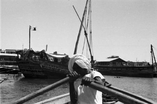 Viaggio in Africa. Massaua: portuale indigeno mentre rema. Imbarcazioni ormeggiate sullo sfondo