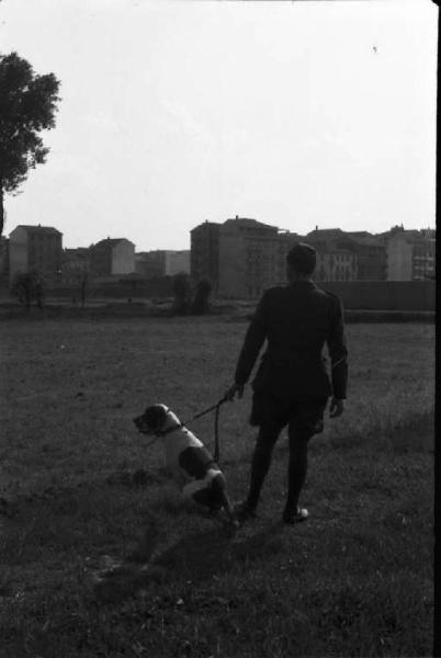 Periferia di Milano: militare in divisa porta a passeggio il cane tra i prati a ridosso dei caseggiati