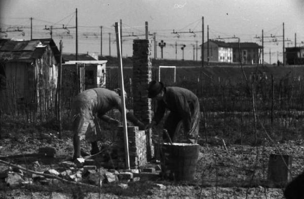 Periferia di Milano: un uomo e una donna al lavoro negli orti di guerra a ridosso della città