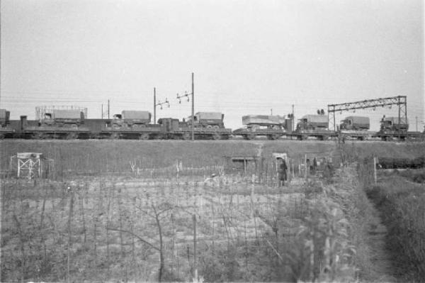 Periferia di Milano: orti di guerra a ridosso della massicciata della ferrovia. Un treno merci in transito