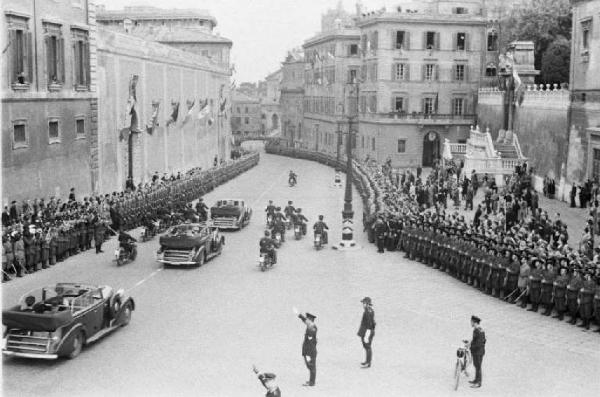 Patti di Roma. Piazza del Quirinale: ripresa dall'alto delle macchine componenti il corteo diplomatico, affiancate da motociclisti, che sfilano tra militari schierati