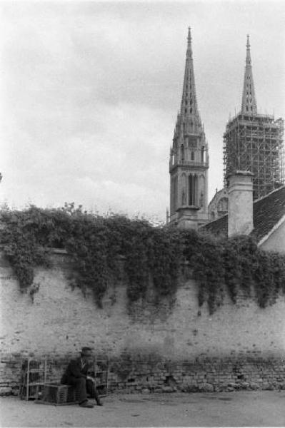 Viaggio in Jugoslavia. Zagabria: un uomo seduto su una panchina nei pressi di un alto muro di cinta. In secondo piano i campanili gemelli della cattedrale