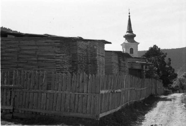 Viaggio in Jugoslavia. Vhrovine: cataste di assi  circoscritte da una staccionata. Sullo sfondo il campanile a cipolla della chiesa