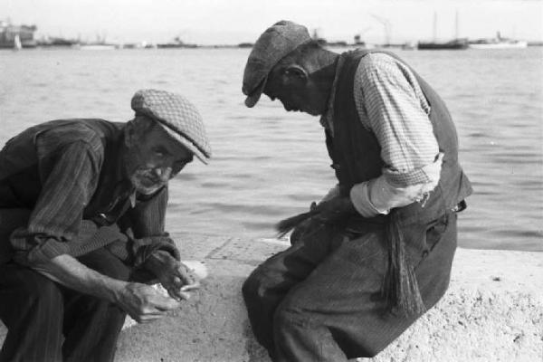 Viaggio in Jugoslavia. Sebenico: coppia di anziani pescatori prepara le esche su un muretto nei pressi del porto