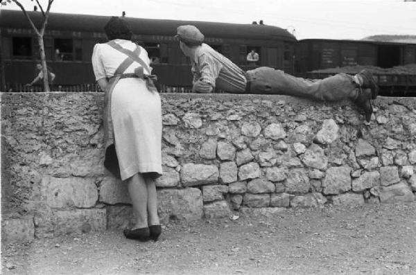 Viaggio in Jugoslavia. Verso Spalato: una coppia di fidanzati osserva il passaggio del convoglio ferroviario sdraiati sopra un muretto adiacente i binari