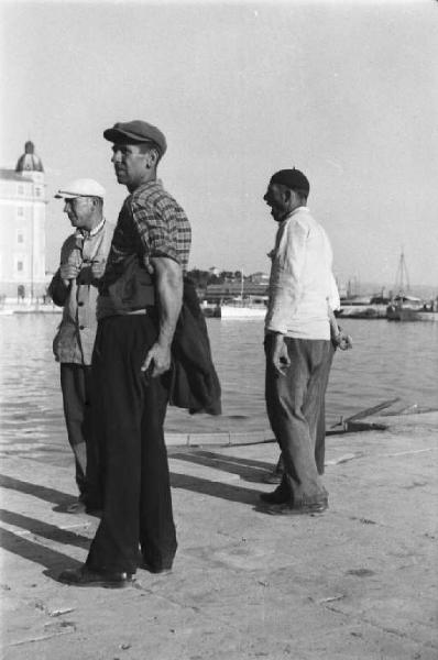 Viaggio in Jugoslavia. Spalato: tre uomini guardano il mare alla banchina del porto