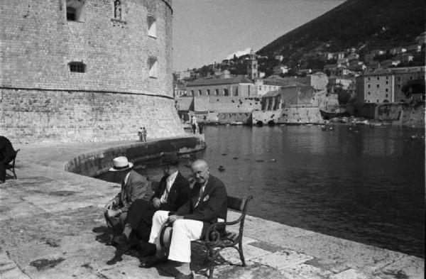 Viaggio in Jugoslavia. Dubrovnik (Ragusa): scene di vita quotidiana - gruppo di uomini anziani seduto su una panchina in riva al mare lungo le mura della città