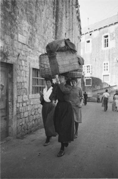 Viaggio in Jugoslavia. Dubrovnik (Ragusa): scene di vita quotidiana - coppia di donne che trasporta ceste appoggiandole sulla testa