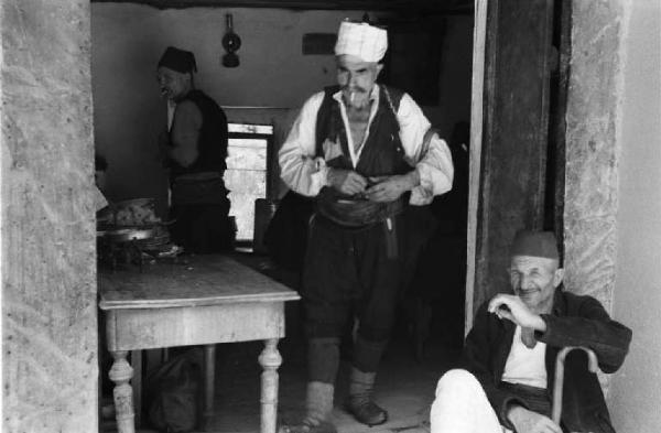 Viaggio in Jugoslavia. Mostar: scene di vita quotidiana - gruppo di uomini sulla soglia e all'interno di un'abitazione