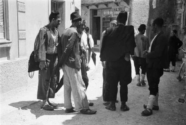 Viaggio in Jugoslavia. Mostar: scene di vita quotidiana - gruppo di uomini che chiacchierano lungo una strada del paese